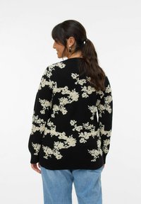 Pull noir avec un motif floral crème texturé, col rond et manches longues, associé à un jean bleu clair.