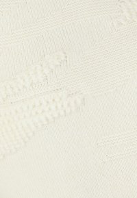 Tissu tricoté crème clair présentant des motifs en relief texturés et des rayures horizontales. Texture douce avec un motif de point uniforme.