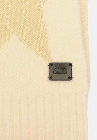 Pull en tricot couleur crème avec une texture duveteuse, présentant un motif géométrique. Comprend une étiquette AllSaints noire avec des accents métalliques.
