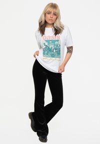 White graphic t-shirt featuring "Oasis" text and a teal illustration. Paired with black flared velvet pants and black boots.