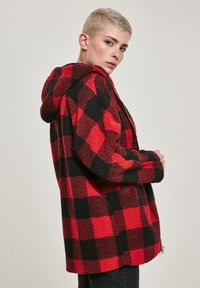 Rdeča in črno karo flis jakna s kapuco, z mehko, teksturirano zunanjostjo in zadrgo na spodnjem robu.