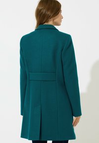 Cappotto in lana verde acqua con colletto strutturato, dettagli della cucitura posteriore e una silhouette elegante. Presenta tasche laterali e una vestibilità sartoriale.