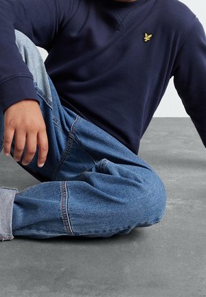 Felpa blu navy con collo tondo e polsini a costine, abbinata a jeans in denim azzurro chiaro con vestibilità rilassata e dettagli di cucitura visibili.