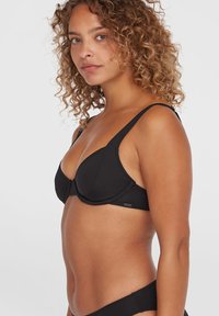 Top bikini nero con ferretto, in tessuto morbido, coppe triangolari, spalline regolabili e una piccola etichetta con logo sul lato.
