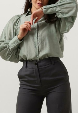 Camisa abotonada verde claro con mangas abullonadas, combinada con pantalones gris oscuro ajustados. Textura suave, diseño minimalista y detalles sutiles.