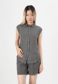 Grå ermeløs skjorte med knappestolpe i front, krage og buet kant, sammen med matchende grå shorts. Laget av teksturert stoff.