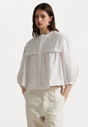 White blouse with puffed sleeves, oversized collar, and front button closure. Smooth cotton fabric with subtle textured details.