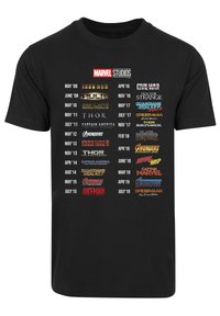Black t-shirt featuring various Marvel Studios logos in white, yellow, red, and gold, arranged chronologically with release dates.
