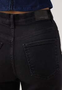 Svarta denimjeans med en slät yta, som har två bakfickor och en midjebandsetikett som säger "perfekta jeans."