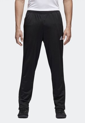 Mand iført sorte Adidas træningsbukser med elastik i taljen og lynlåse ved anklerne, kombineret med sorte sko og en hvid skjorte.