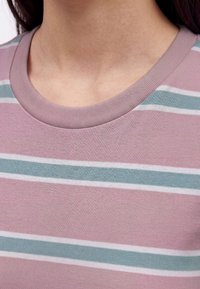 Primo piano di una persona che indossa una maglietta a righe rosa, blu e bianca con scollo a girocollo che mostra il collo e la parte superiore del petto.