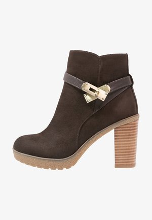 Bruine suède enkellaars met een donker leren riem en metalen gespdetail. Voorzien van een gestructureerde lichtbruine blokhak en een rubberen zool.