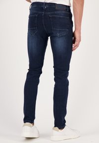 Dark blue denim jeans with a slim fit, medium rise, and back pockets. Features a textured finish and subtle fading details.