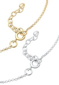 Guld- och silverkedjor i interlock med cirkulära länkar och ett spänne, som har varierande länkstorlekar och polerade ytor.