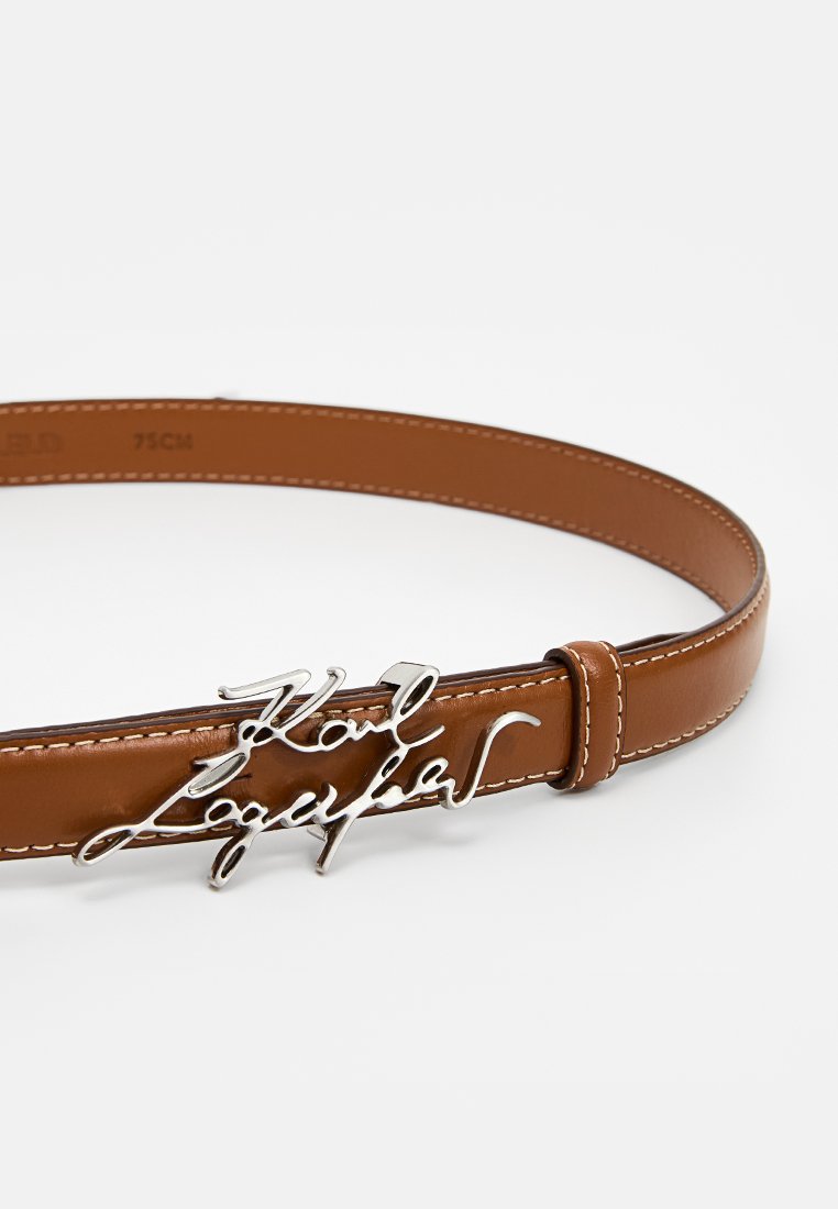 Ceinture en cuir marron avec une boucle logo en métal argenté au lettrage en cursive, rehaussée de coutures blanches le long des bords.