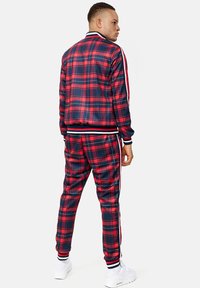 Red and navy plaid tracksuit with white stripe accents, featuring a zippered jacket and elastic waistband on pants, made of smooth material.