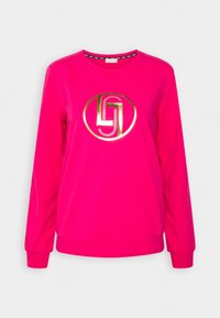 Fuchsiová mikina s dlouhými rukávy, která má kovově zlaté kruhové logo a kontrastní černý límec s tištěným textem.