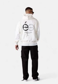 White hoodie featuring a black graphic design on the back, paired with black cargo pants and white sneakers. Simple, clean design.
