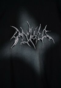 Czarna tkanina z jaggedowym, srebrnym logo. Tekstura jest gładka z półmatowym wykończeniem, ukazując kontrastowy wzór.