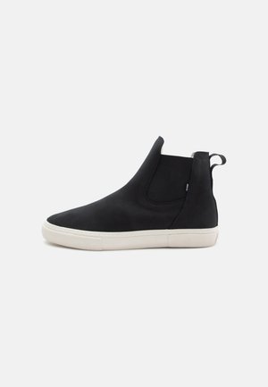 Black slip-on ankle boot made of smooth material, featuring a white rubber sole and elastic side panels. Loop tab on the heel for easy wear.