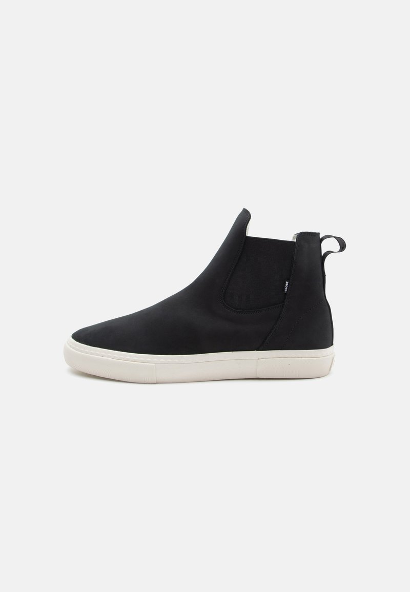 Botín negro tipo slip-on até con material suave, con suela de goma blanca y paneles laterales elásticos. Lengüeta en el talón para ponérselo fácilmente.