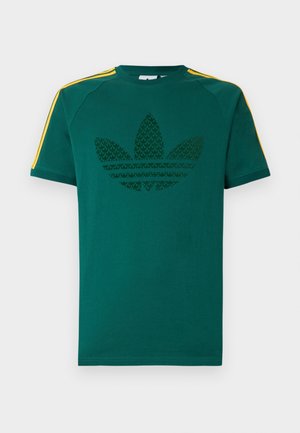 Zöld rövid ujjú póló sötétzöld Adidas trefoil logóval és sárga csíkokkal a vállakon, fehér háttér előtt.