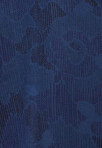 Tessuto blu strutturato con un sottile motivo floreale, caratterizzato da una trama diagonale. Il colore varia da un blu navy profondo a tonalità di blu più chiare.