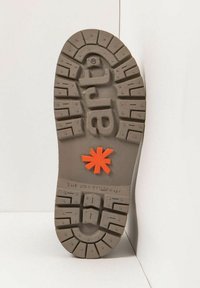 Suela de un zapato de goma gris con surcos profundos. Presenta un acento en forma de estrella naranja en el centro con texto en relieve que dice "THE ART COMPANY."