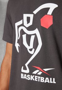 Grå t-shirt med et stort hvidt grafik af en basketballspiller og teksten "BASKETBALL" i fed hvid, med rød accent og logo.