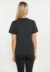 Tricou negru cu mâneci scurte, fabricat dintr-un material moale și neted. Dispune de un decolteu rotund și o siluetă ajustată, asortat cu colanți negri.