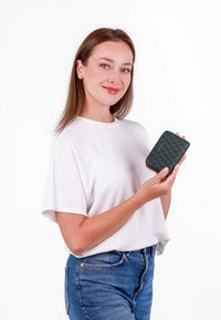 Peněženka v tmavě zelené barvě s texturovaným vzorem, se zipem a zlatým logem, kterou drží osoba v bílém tričku a modrých džínách.