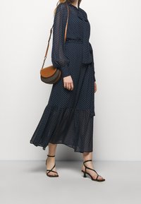 Námořnické šaty s puntíky, se střihnutým korzetem, dlouhými rukávy a vrstvenou sukní; doplněné o hnědou crossbody kabelku a černé sandály na podpatku.
