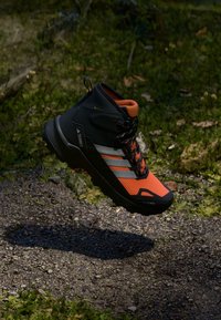 Czarno-pomarańczowy but trekkingowy z teksturowanym meshowym wierzchem, wyraźnymi sznurówkami i odporno-ruggedową podeszwą, zaprojektowany do aktywności na świeżym powietrz. 