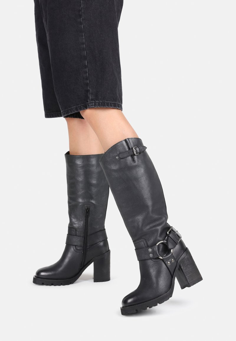 Black leather knee-high boots with a chunky heel, side zip, and decorative straps with buckles. Textured finish and sturdy sole.