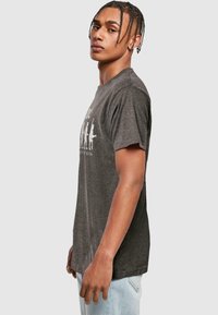 Grå kortærmet t-shirt i blødt stof, med et hvidt grafisk motiv der viser en progression af rockfigurer. Rund hals og afslappet pasform.