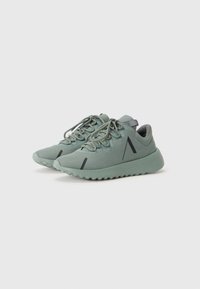 Las zapatillas deportivas de color verde menta tienen una parte superior texturizada, punta redondeada y una suela gruesa y ondulada. Se pueden ver detalles en negro en los costados.