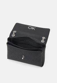 Sort læderhåndtaske med præget mønster, sølv hardware og en CK-logo på toppen. To rum indeni, slankt design og klaplukning.