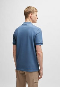 Koszulka polo w niebieskim kolorze, z krótkimi rękawami, wykonana z gładkiego materiału. Posiada klasyczny kołnierzyk i prosty dół, bez widocznych logo.