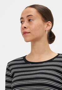 Black and white striped long-sleeve shirt with a rounded neckline, made of a ribbed fabric. Silver hoop earrings accent the model's look.