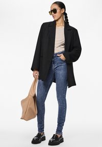 Svart oversized blazer over en stripete skjorte, kombinert med h�øygrinsede denimjeans og store svarte loafers. Tilbehøret inkluderer en beige veske.