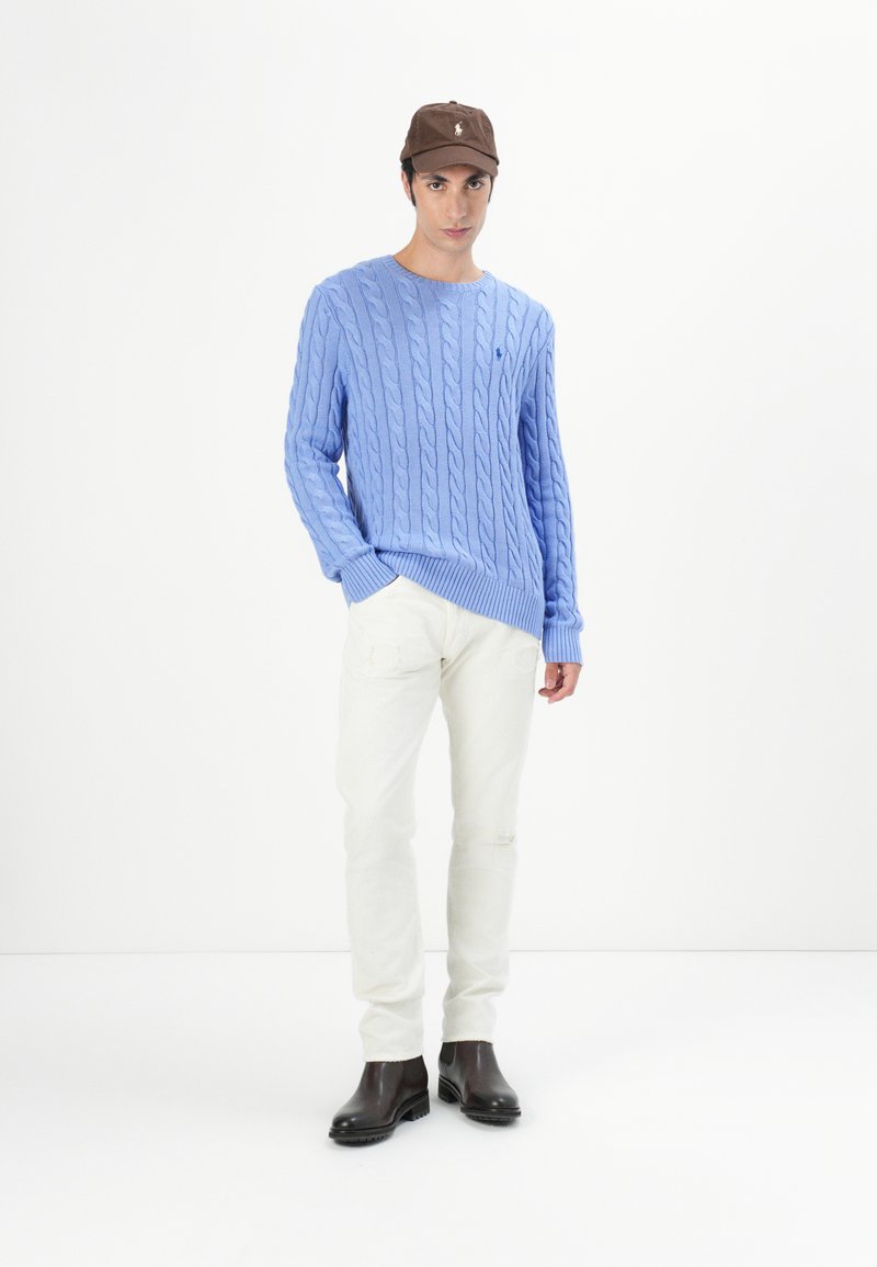 Maglione a costine blu chiaro, pantaloni chinos crema e stivali alla caviglia in pelle marrone. Il modello indossa un berretto marrone con un accento di logo.