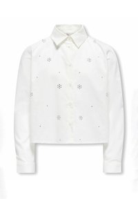 Camicia bianca corta con maniche lunghe, polsini a coste, chiusura con bottoni e decorazioni di borchie argentate a forma di fiori.