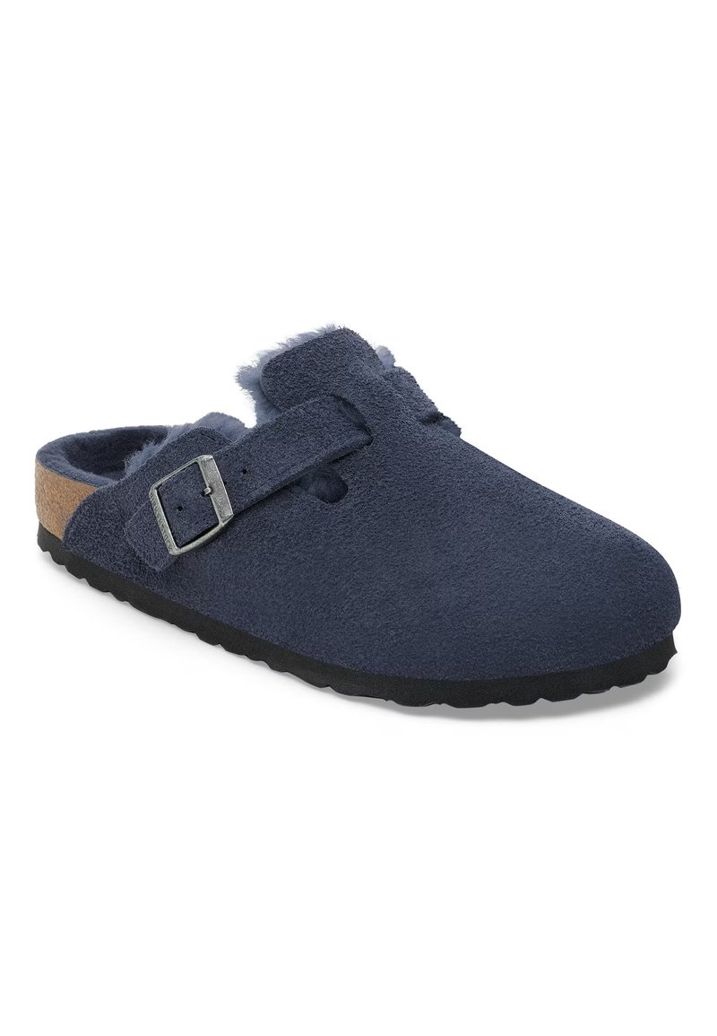 Marineblaue Clogs aus weichem Wildleder, mit einer Schnalle, flauschigem Futter und einer strukturierten Gummisohle. Offenes Design für ein einfaches Hineinschlüpfen.