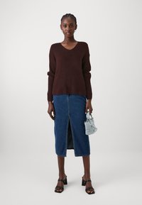 Brauner V-Ausschnitt-Pullover, blaue Jeansrock mit einem Schlitz vorne, schwarze Sandalen mit Blockabsatz und eine hellblaue Mini-Handtasche. Glatte Texturen durchgehend.