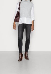 Pull en maille gris à col roulé porté sur une chemise blanche à col, associé à un jean noir et des bottines marron à talons. Accent avec un sac bordeaux.