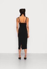 Svart figursydd midiklänning med tunna spagettiremmar, featuring en dragkedja i ryggen och en slits i fållen, tillverkad av ett mjukt, elastiskt tyg.