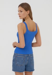 Top a canotta a costine blu royal con spalline larghe, abbinato a pantaloni shorts in denim chiaro con dettagli strappati e orlo sfrangiato.