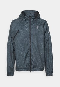 Veste à capuche zippée gris foncé avec un motif tacheté subtil, logo NBA sur la poitrine, et logo Nike sur la manche gauche.