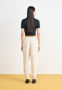 Črna skrajšana majica, bež trenirke z elastičnim pasom in črne čevlje. Gladka tekstura, udoben kroj in nevtralna barvna paleta.