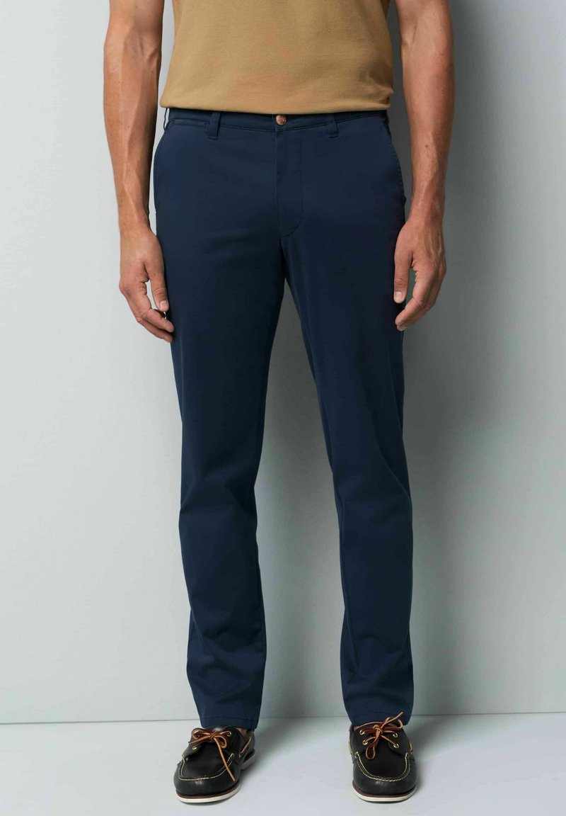 Navy blue tailored pants with a smooth texture, front pockets, and a button closure. Paired with black shoes featuring brown laces.